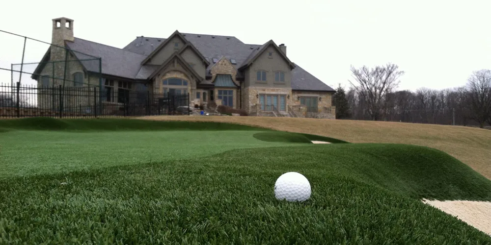 A personal putting green in a home's backyard, featuring realistic artificial turf and sand bunkers, perfect for golf enthusiasts looking to practice their game.
